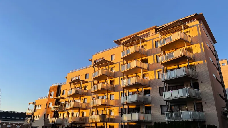 Moderne boligblokk med glassbalkonger, badet i gyllent sollys under blå himmel.