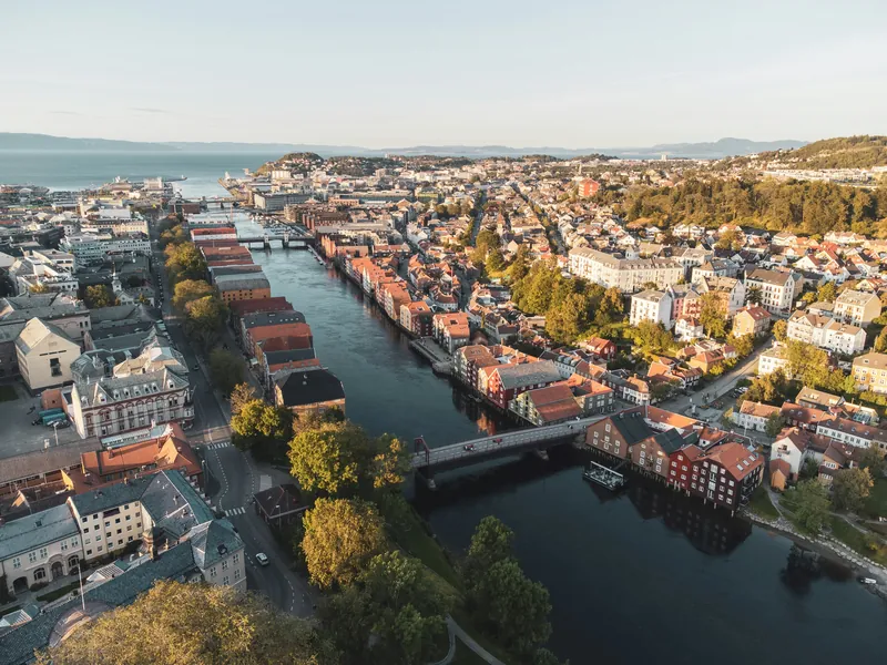 Trondheim sett fra lufta i lavt sollys, med fargerike bryggehus langs Nidelva, Gamle Bybro og fjorden i bakgrunnen.